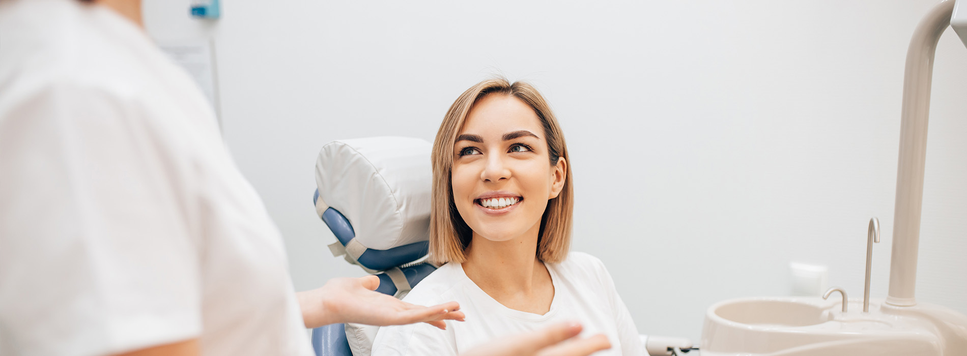 A person is seated in a dental chair, receiving care from a dental professional who stands behind them.