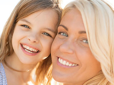 A woman and a young girl smiling at the camera, capturing a joyful family moment.
