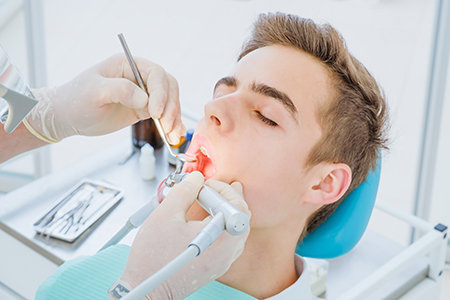 The image depicts a dental setting where a patient is seated in a chair, receiving dental care from a professional.