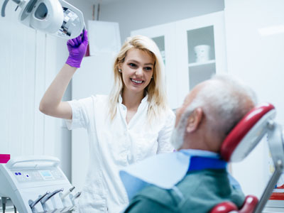 The image depicts a dental professional assisting an elderly patient in a dental chair.
